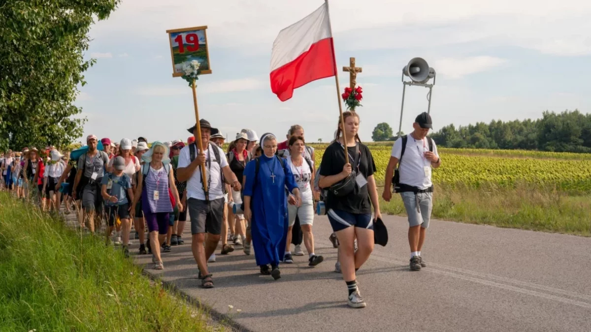 Pielgrzymi idący drogą z flagami i krzyżem podczas Pieszej Pielgrzymki Tarnowskiej.