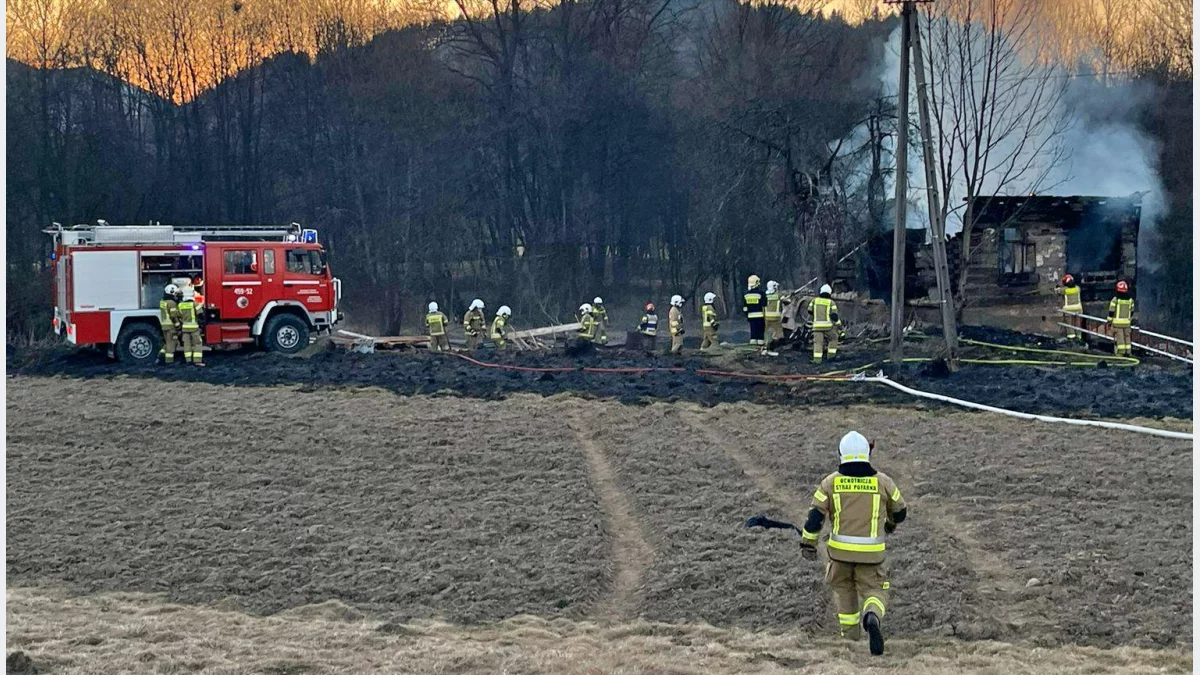 Strażacy gaszący pożar drewnianego budynku i suchej trawy w miejscowości Dobra