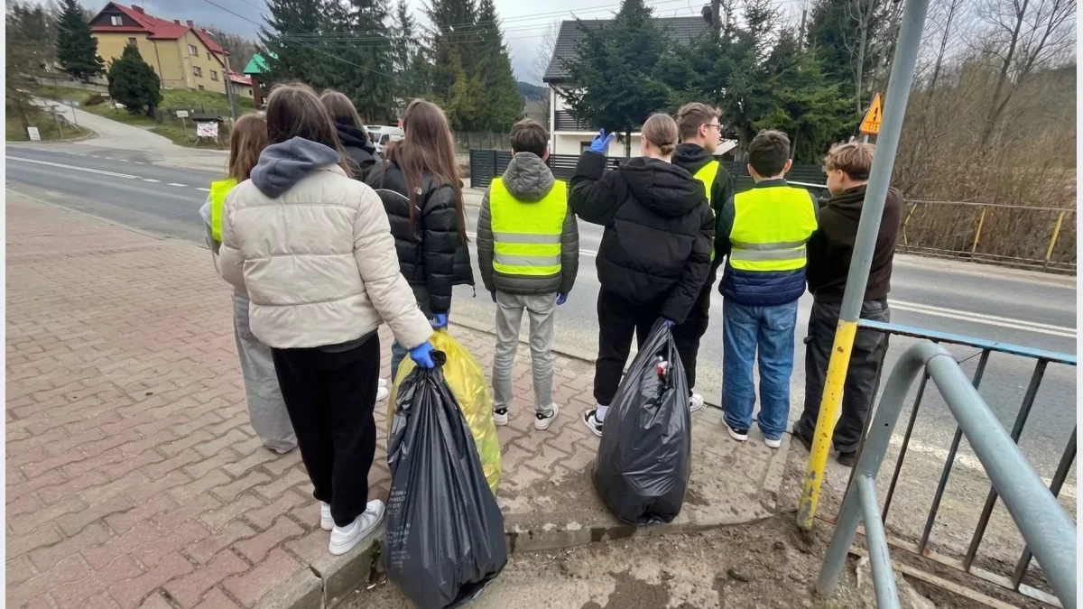 Mieszkańcy gminy Mszana Dolna podczas sprzątania brzegów potoku, ubrani w kamizelki odblaskowe i wyposażeni w worki na odpady.