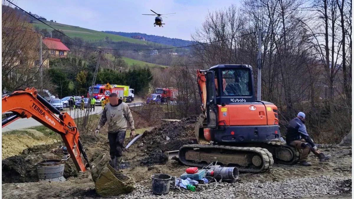 Miejsce wypadku w Kamionce Małej, strażacy obok sprzętu budowlanego, w tle lądujący śmigłowiec LPR