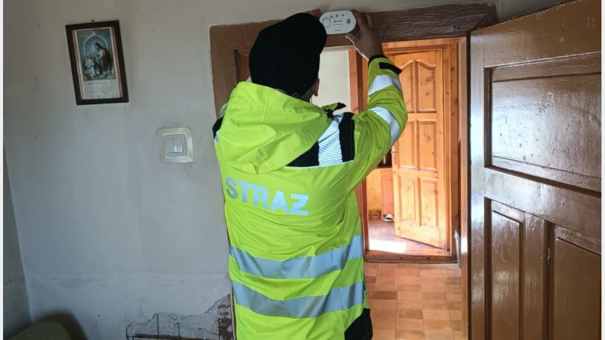 Strażak ochotnik montujący czujnik tlenku węgla na ścianie w budynku mieszkalnym.