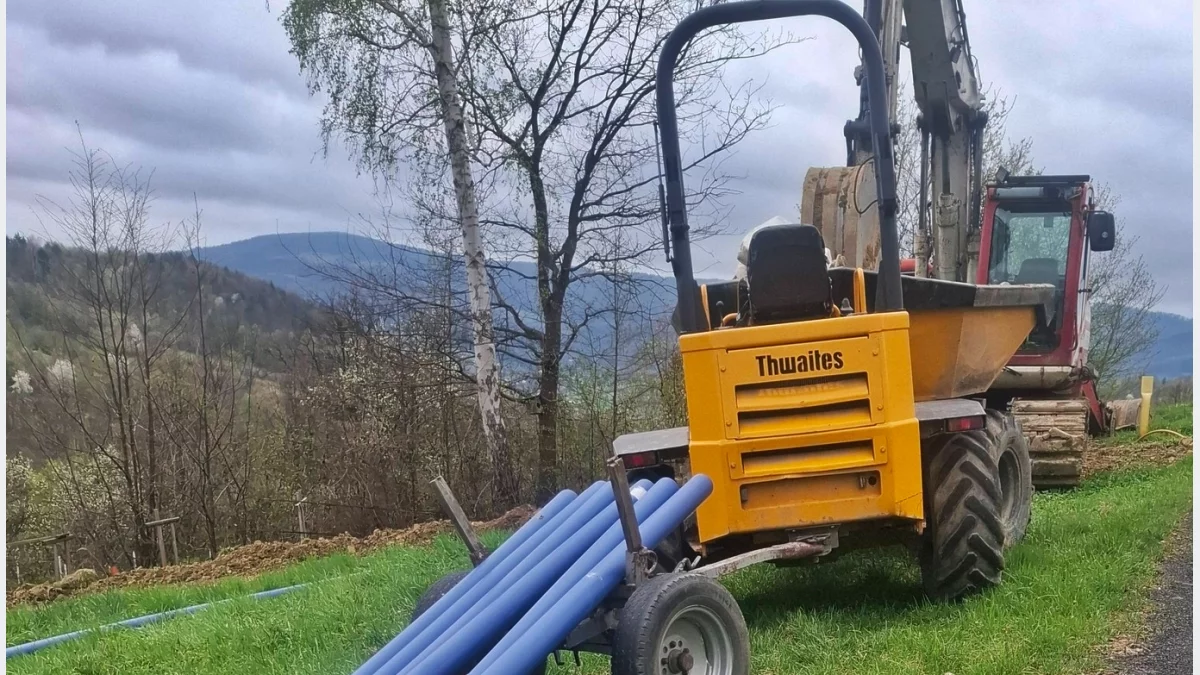 Prace ziemne przy budowie sieci kanalizacyjnej na terenie wiejskim, sprzęt budowlany i rury przygotowane do montażu